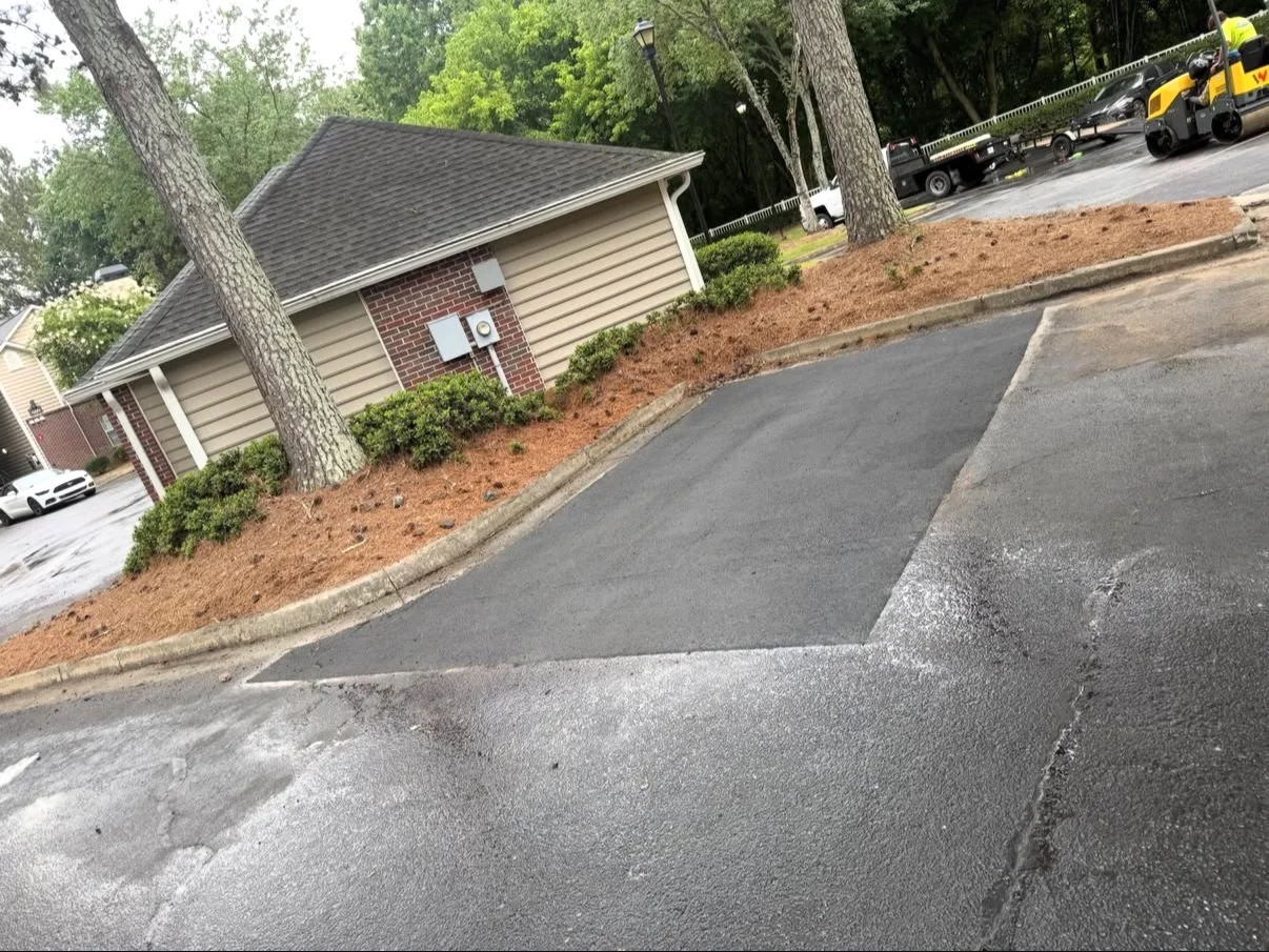 Newly paved black asphalt driveway with concrete edging and mulch landscaping