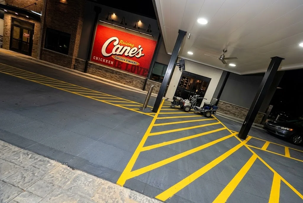 Dark gray sealed asphalt parking lot with bright yellow striping, parking space lines, and directional arrows