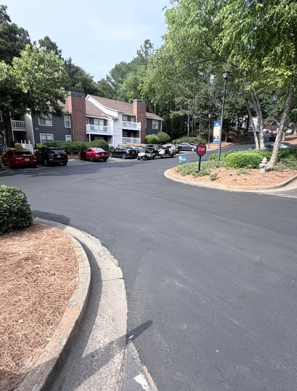 Newly paved asphalt parking lot with concrete curbing, mulch landscaping, and mature trees