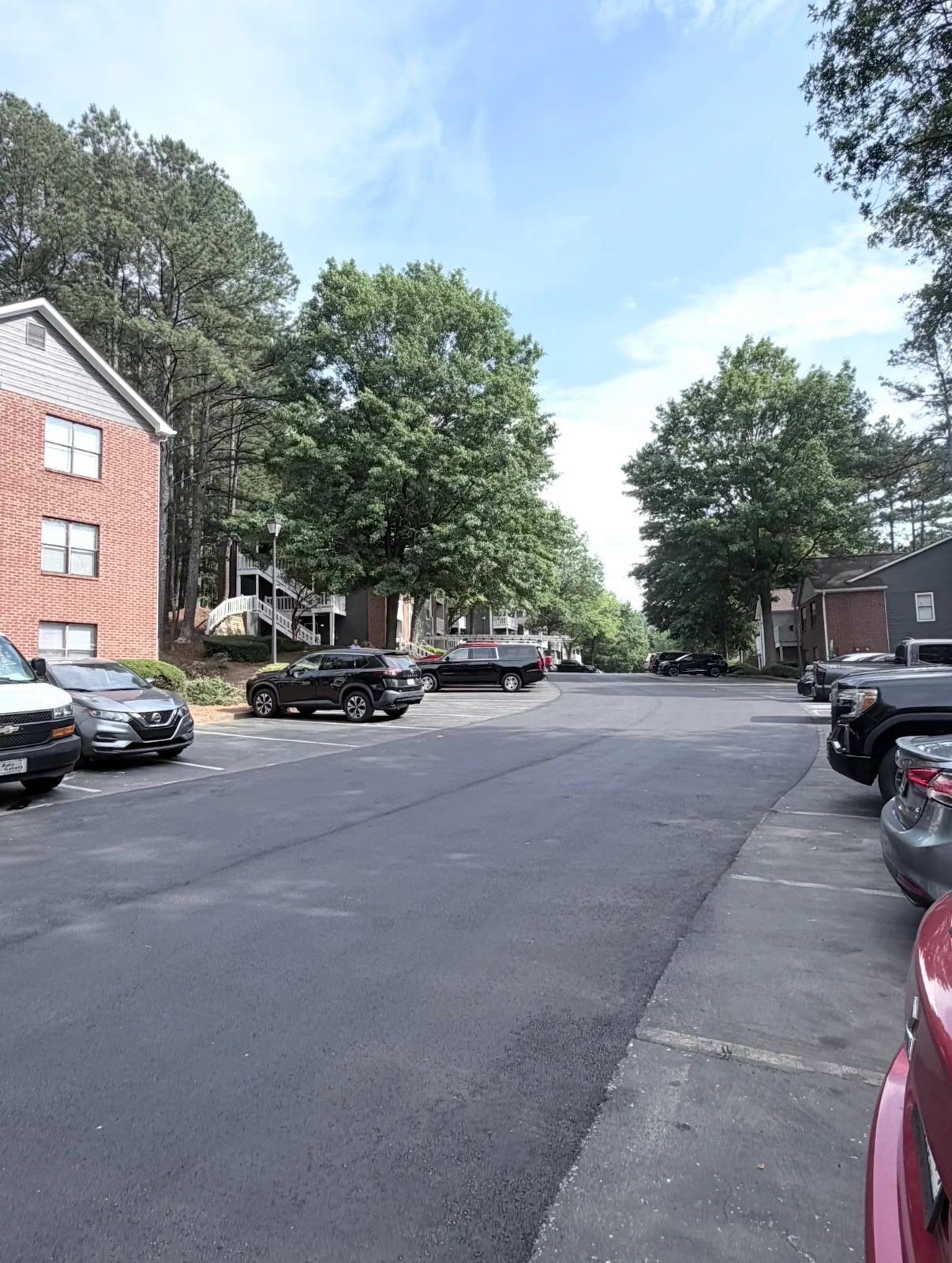 Newly paved asphalt parking lot with marked spaces, concrete curbs, and brick residential buildings